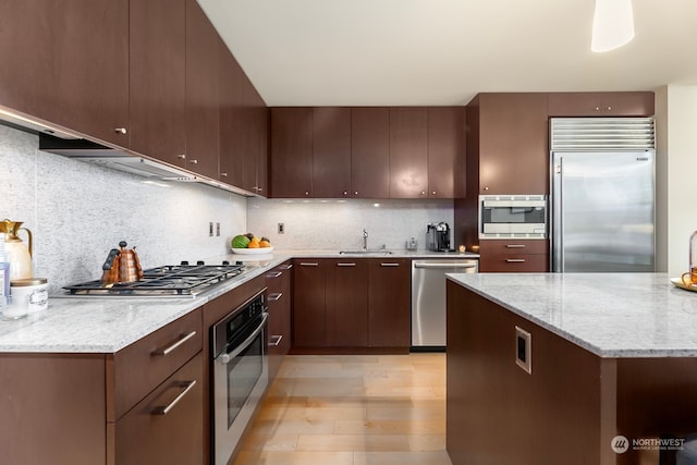 kitchen with decorative backsplash, dark brown cabinets, light stone countertops, light wood-type flooring, and built in appliances