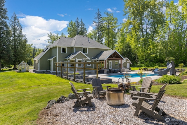 rear view of property with a yard, an outdoor structure, and a fire pit