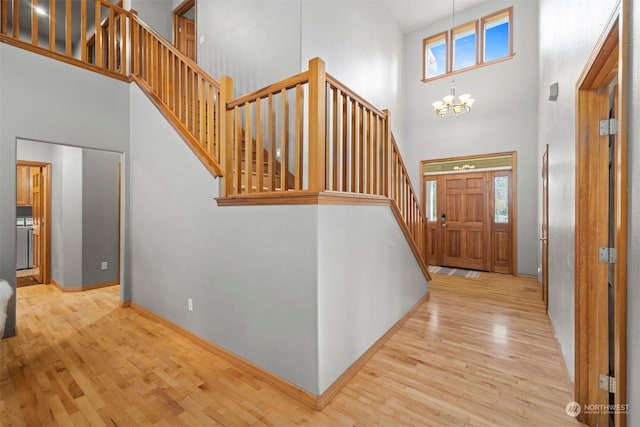 entrance foyer with a notable chandelier, a towering ceiling, a wealth of natural light, and light wood-type flooring