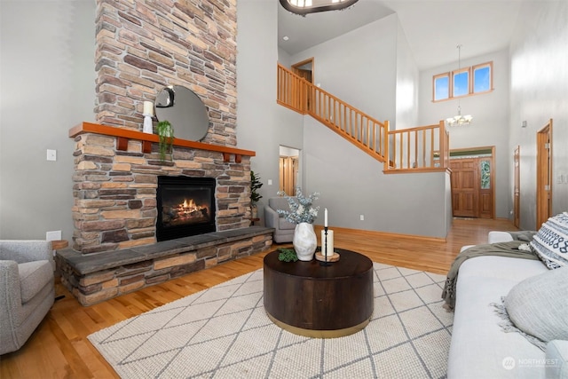 living room with a towering ceiling, a chandelier, a fireplace, and light hardwood / wood-style floors