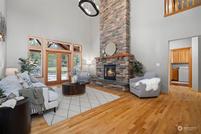 living room with a stone fireplace, a towering ceiling, and light hardwood / wood-style flooring