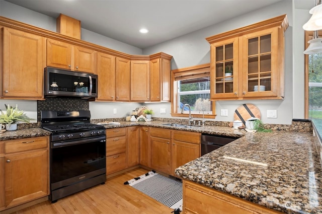 kitchen with dark stone countertops, sink, black appliances, and light wood-type flooring