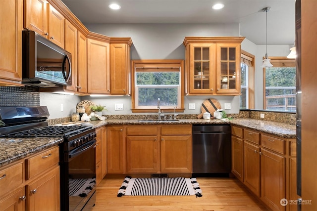 kitchen with sink, decorative light fixtures, a wealth of natural light, dark stone counters, and black appliances