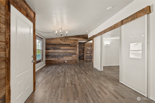 unfurnished living room featuring wood walls, a textured ceiling, lofted ceiling, dark wood-type flooring, and an inviting chandelier