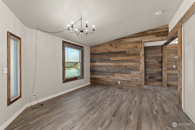 unfurnished dining area with wooden walls, vaulted ceiling, dark wood-type flooring, and a textured ceiling