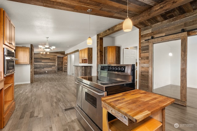 kitchen featuring a barn door, stainless steel appliances, wooden walls, dark wood-type flooring, and a notable chandelier