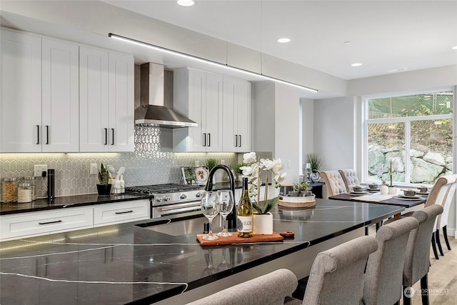 kitchen featuring white cabinetry, decorative backsplash, high end range, and wall chimney exhaust hood