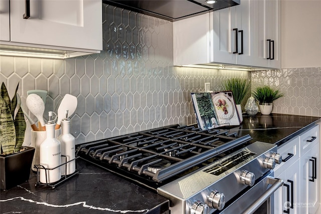 kitchen featuring stainless steel gas range, ventilation hood, white cabinets, decorative backsplash, and dark stone counters