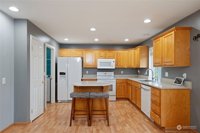 kitchen featuring a breakfast bar area, a kitchen island, light wood-type flooring, sink, and white appliances