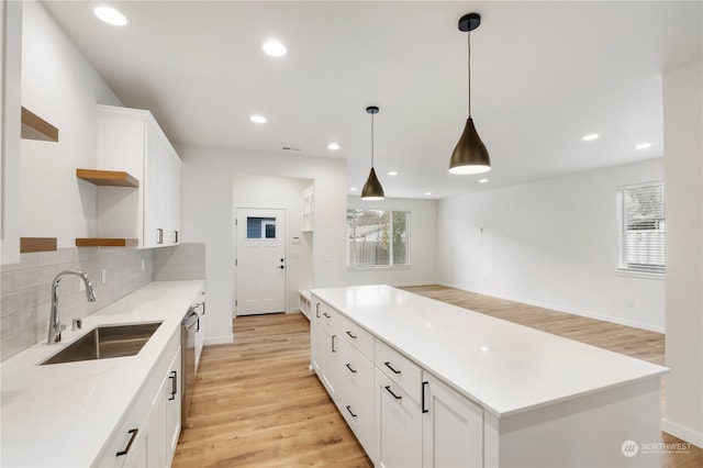 kitchen with decorative backsplash, white cabinetry, light stone countertops, light wood-type flooring, and sink