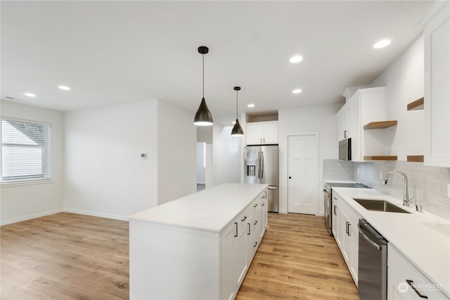 kitchen with a kitchen island, sink, white cabinets, appliances with stainless steel finishes, and light hardwood / wood-style floors