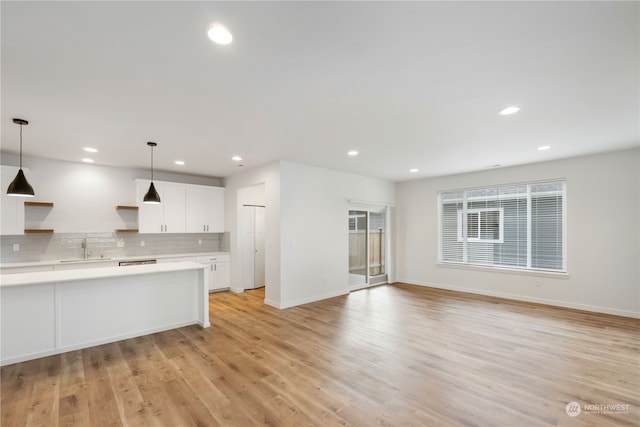 kitchen featuring sink, hanging light fixtures, white cabinets, decorative backsplash, and light hardwood / wood-style flooring