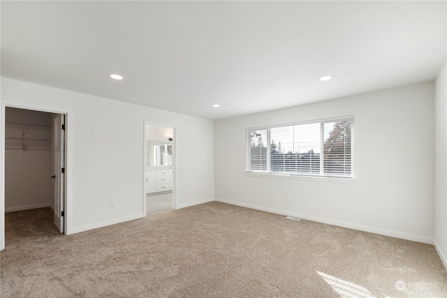 unfurnished bedroom featuring light carpet, a walk in closet, a closet, and ensuite bath