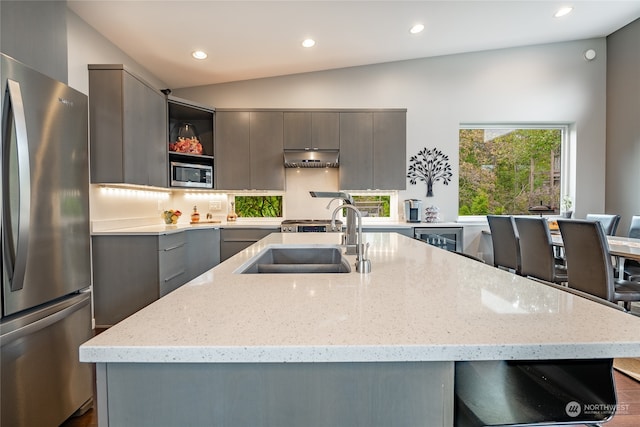 kitchen featuring gray cabinetry, stainless steel appliances, sink, vaulted ceiling, and light stone counters