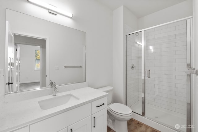 bathroom featuring a shower with door, vanity, wood-type flooring, and toilet