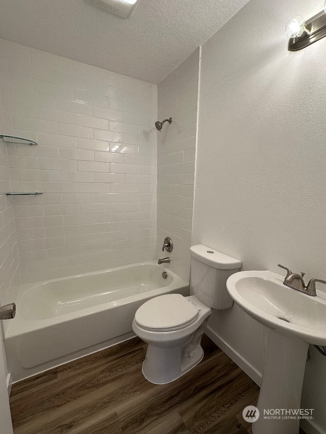 bathroom with toilet, wood-type flooring, a textured ceiling, and tiled shower / bath