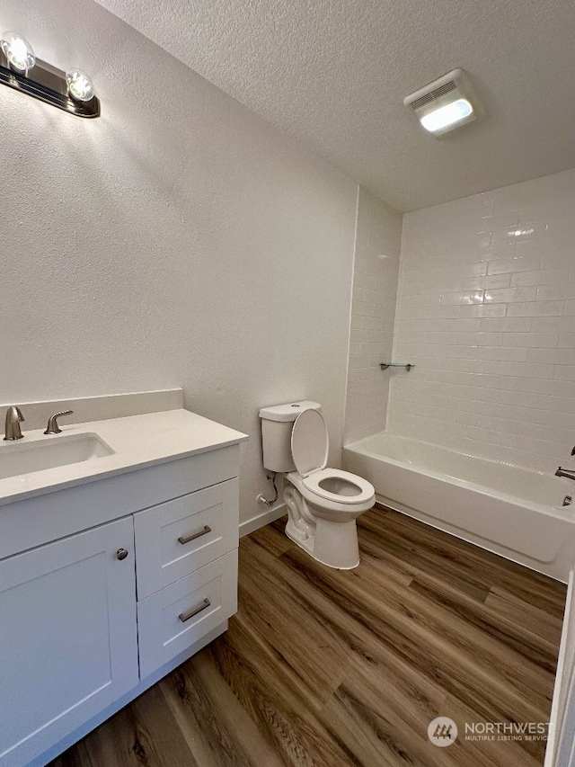 full bathroom featuring a textured ceiling, hardwood / wood-style floors, toilet, tiled shower / bath, and vanity