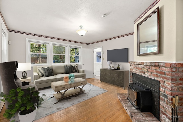 living room with ornamental molding, light hardwood / wood-style flooring, a brick fireplace, and a textured ceiling