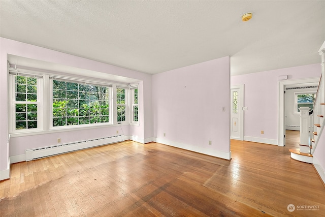 empty room featuring a wealth of natural light, a baseboard radiator, and wood-type flooring