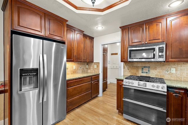 kitchen with appliances with stainless steel finishes, a textured ceiling, light stone countertops, light hardwood / wood-style flooring, and crown molding