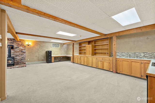 unfurnished living room with built in features, a wood stove, beamed ceiling, and light colored carpet