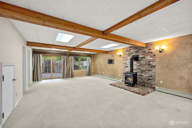 unfurnished living room with beam ceiling, a wood stove, a baseboard radiator, and light colored carpet