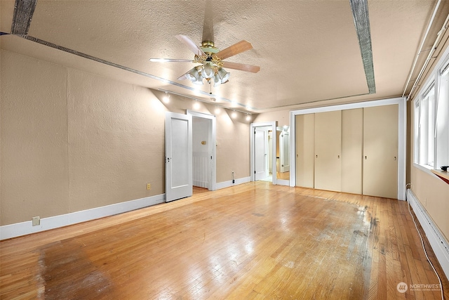 unfurnished bedroom with light hardwood / wood-style flooring, a textured ceiling, a baseboard radiator, and ceiling fan