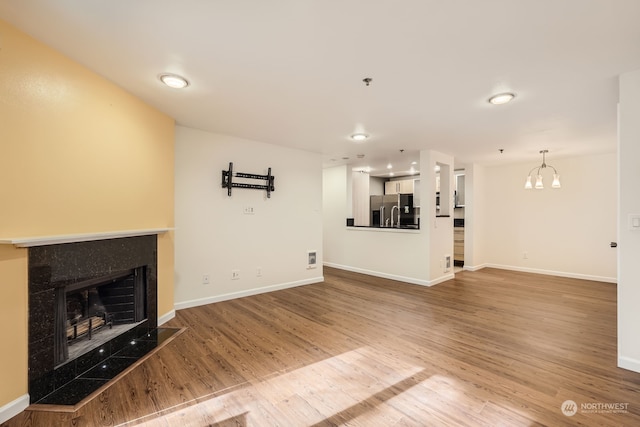 unfurnished living room with a fireplace, a notable chandelier, and wood-type flooring