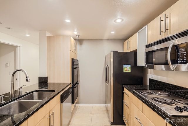 kitchen featuring dark stone countertops, light brown cabinetry, appliances with stainless steel finishes, and sink