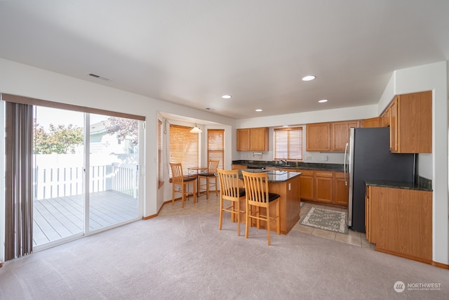 kitchen with sink, a kitchen bar, a center island, stainless steel refrigerator, and light colored carpet