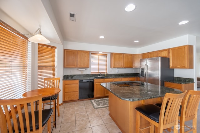 kitchen with black appliances, light tile patterned flooring, sink, a kitchen island, and a breakfast bar