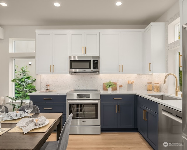 kitchen with sink, light wood-type flooring, blue cabinetry, white cabinetry, and stainless steel appliances