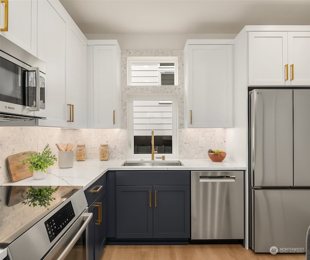 kitchen with appliances with stainless steel finishes, light hardwood / wood-style flooring, white cabinetry, and sink