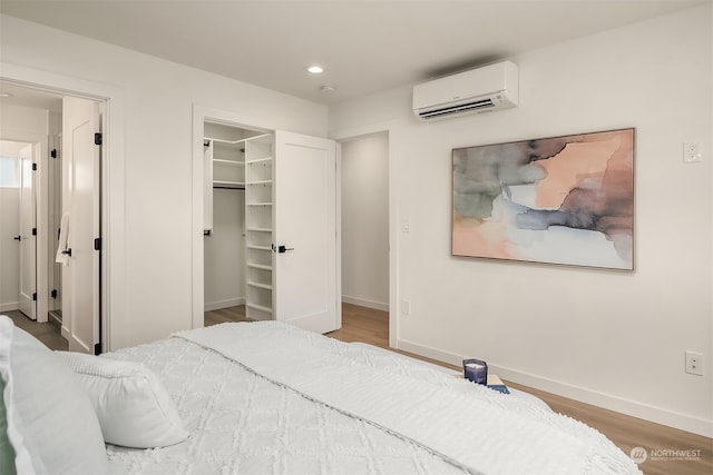 bedroom featuring hardwood / wood-style flooring, a walk in closet, a wall unit AC, and a closet