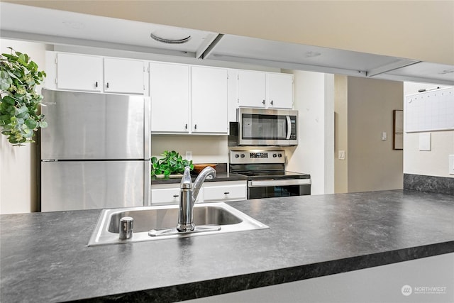kitchen featuring dark countertops, white cabinets, appliances with stainless steel finishes, and a sink