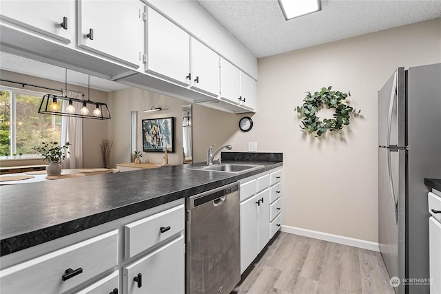 kitchen with appliances with stainless steel finishes, a sink, white cabinetry, dark countertops, and light wood-type flooring