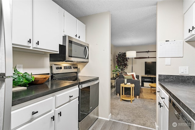 kitchen with light hardwood / wood-style floors, white cabinetry, stainless steel appliances, and a textured ceiling