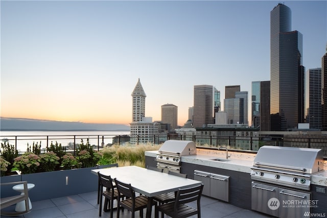 patio terrace at dusk with sink, area for grilling, and a water view