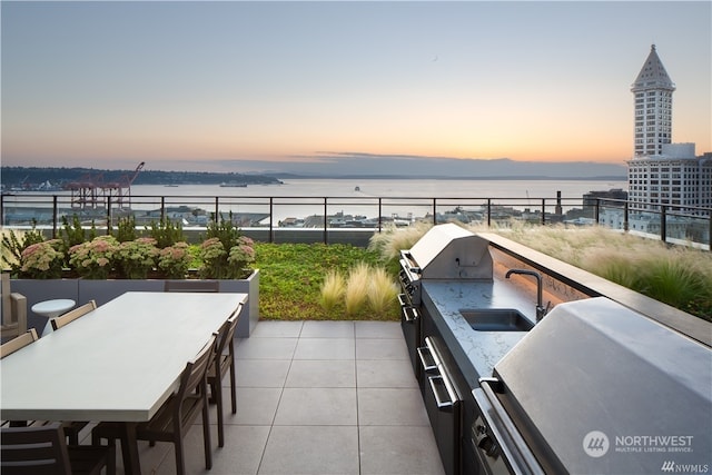 patio terrace at dusk with a water view, area for grilling, and sink