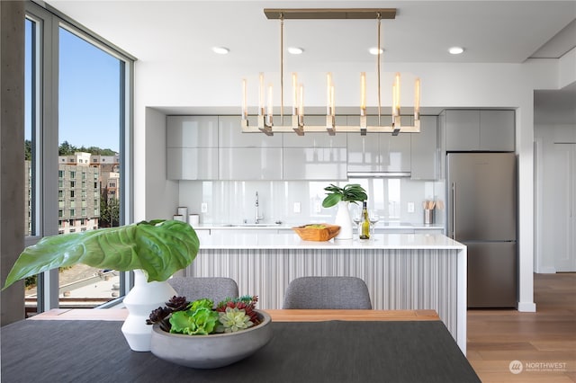 kitchen featuring hardwood / wood-style flooring, hanging light fixtures, stainless steel refrigerator, gray cabinets, and sink