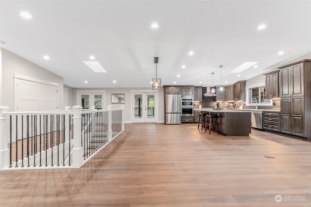 kitchen with stainless steel appliances, wall chimney range hood, a breakfast bar, a skylight, and a center island