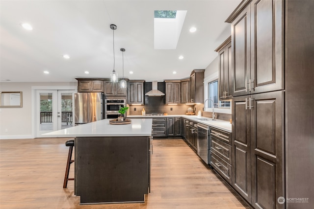 kitchen featuring a center island, wall chimney exhaust hood, hanging light fixtures, a skylight, and appliances with stainless steel finishes