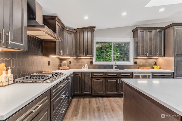 kitchen with light hardwood / wood-style floors, lofted ceiling, stainless steel appliances, wall chimney exhaust hood, and sink