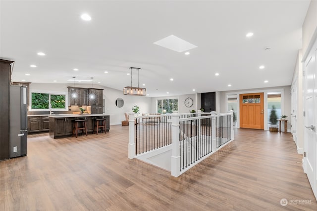 interior space with light hardwood / wood-style floors, a center island, dark brown cabinetry, a skylight, and stainless steel refrigerator