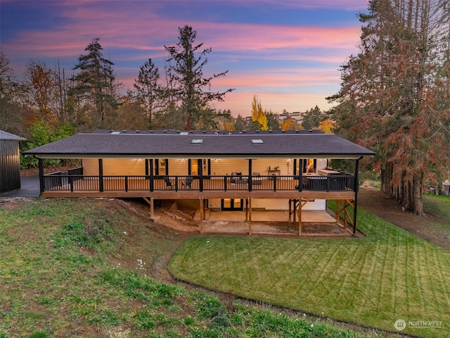 back house at dusk featuring a lawn and a wooden deck