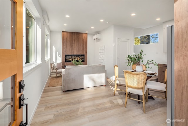 dining space featuring a large fireplace, a wall mounted AC, and light hardwood / wood-style floors