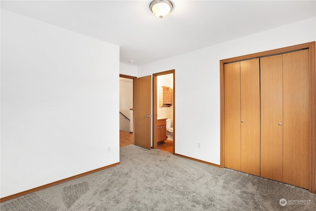 unfurnished bedroom with a closet, ensuite bathroom, and light colored carpet