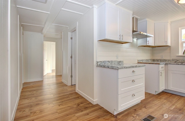 kitchen with wall chimney range hood, light hardwood / wood-style flooring, sink, white cabinets, and light stone counters