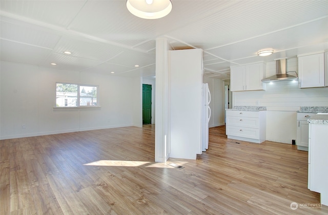 kitchen featuring wall chimney range hood, white cabinetry, light wood-type flooring, white fridge, and light stone counters