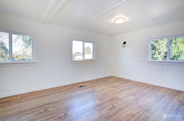 empty room with light hardwood / wood-style flooring and beam ceiling